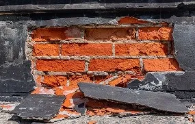 A close-up of a broken brick wall with exposed red bricks and scattered debris.