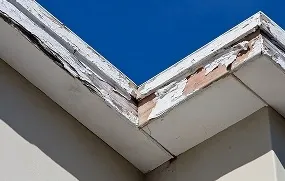 A close-up of a deteriorating white building corner against a clear blue sky.